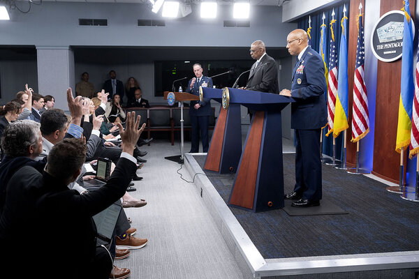 Pentagon officials including Pat Ryder stand at podiums as seated reporters raise their hands to ask questions.